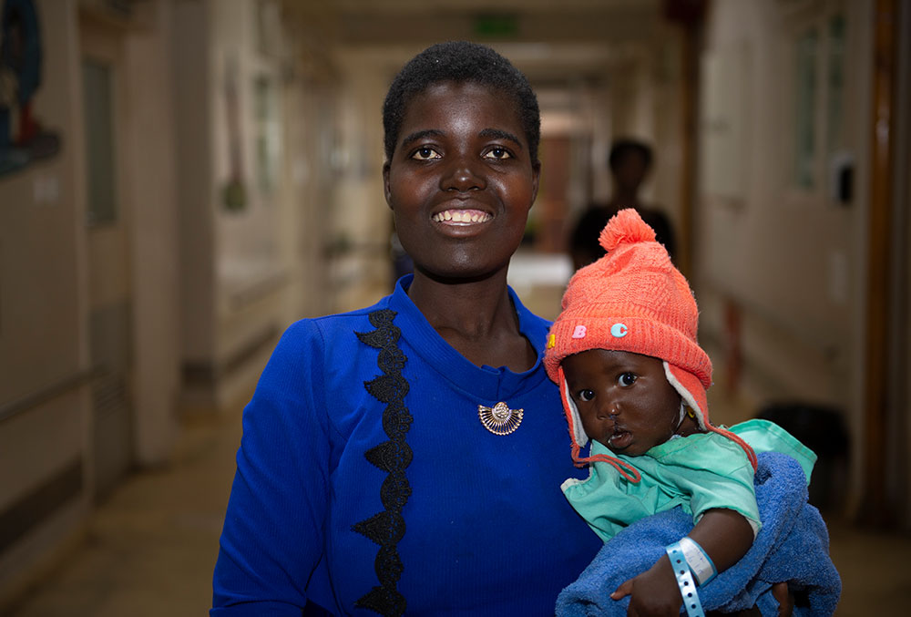 Rosemary smiling and holding Nyasha in the hospital after cleft surgery