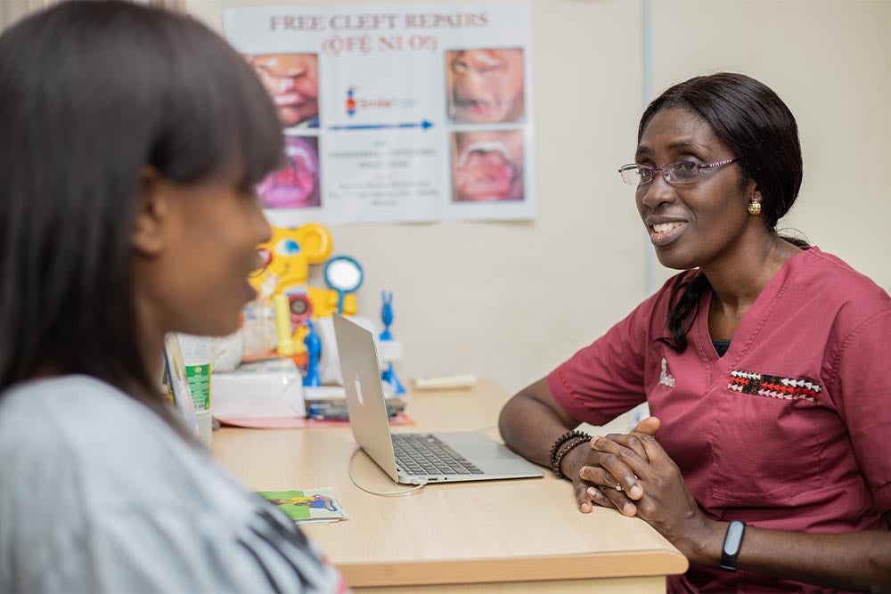 Dr. Adeola Olusanya smiling and speaking with Susannah at her desk