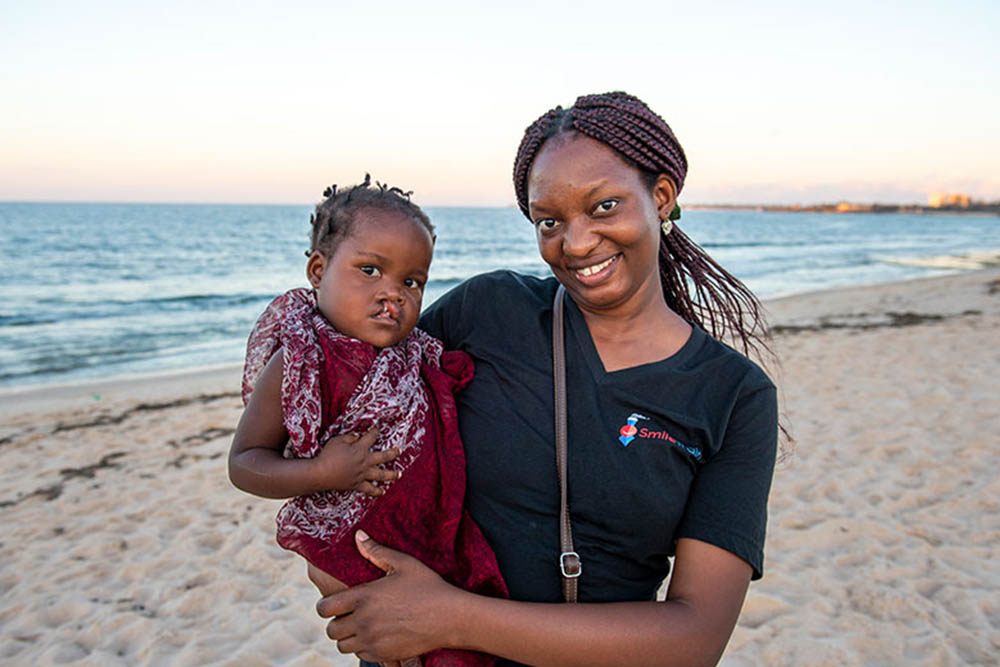 Yona smiling and holding Zena on the beach before her cleft surgery