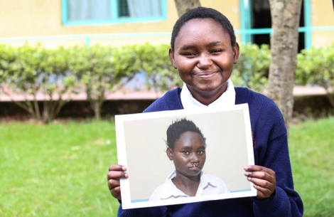 Damaris smiling and holding a photo of herself before cleft surgery