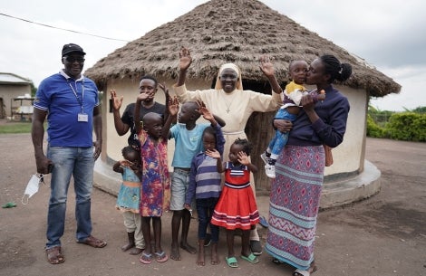 Sister Dr. Liliana Najjuka smiling and raising her hands with Kellen and her son Eric after his cleft surgery