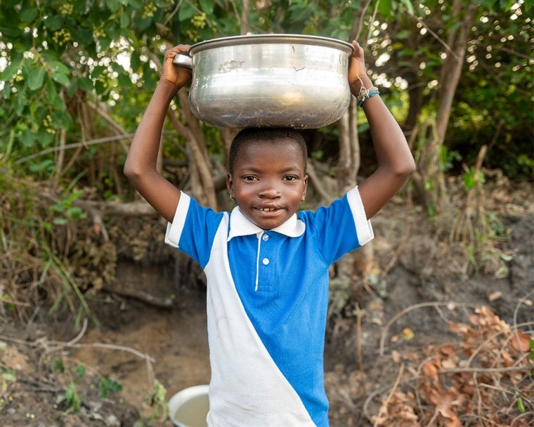 Akuya smiling and carrying water over her head after cleft surgery