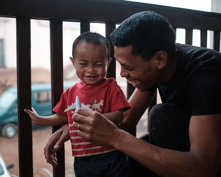 Eden smiling with his father Heriniaina and playing with a toy plane after cleft surgery